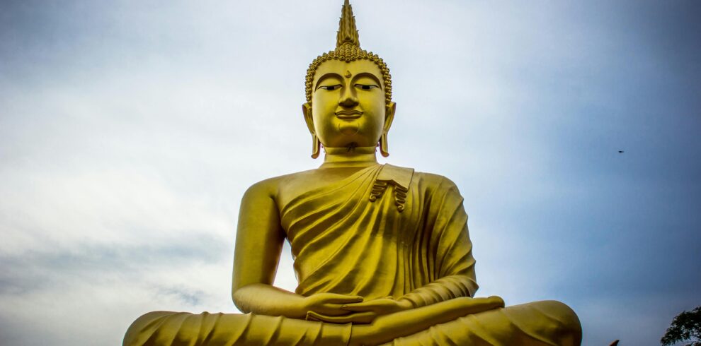 A majestic golden Buddha statue against a serene blue sky, symbolizing peace and spirituality.